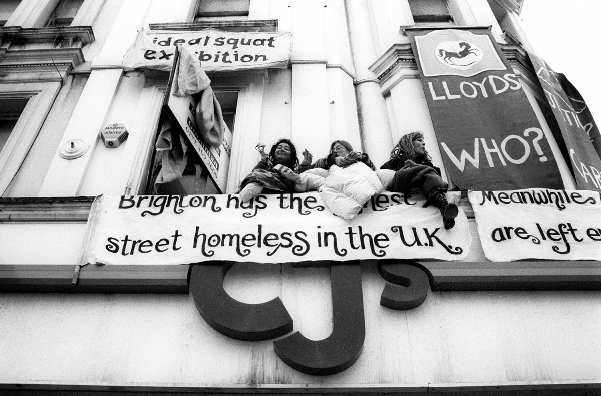 Protesters sit on the upper window ledge of an empty clothing shop squatted by social activists. Titled 'Ideal Squat Exhibition', it was occupied to draw attention to Brighton's high level of homelessness despite all the empty houses around town. Brighton, Sussex, England. Photo: Alec Smart