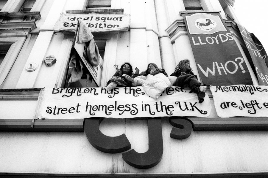 Protesters sit on the upper window ledge of an empty clothing shop squatted by social activists. Titled 'Ideal Squat Exhibition', it was occupied to draw attention to Brighton's high level of homelessness despite all the empty houses around town. Brighton, Sussex, England. Photo: Alec Smart