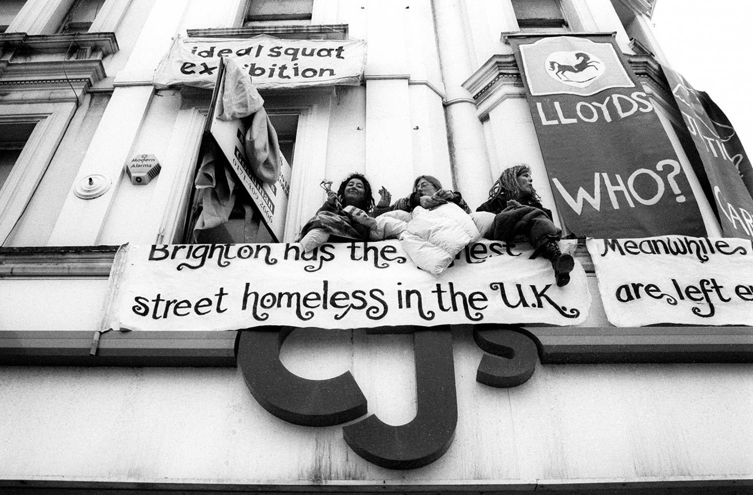 Protesters sit on the upper window ledge of an empty clothing shop squatted by social activists. Titled 'Ideal Squat Exhibition', it was occupied to draw attention to Brighton's high level of homelessness despite all the empty houses around town. Brighton, Sussex, England. Photo: Alec Smart