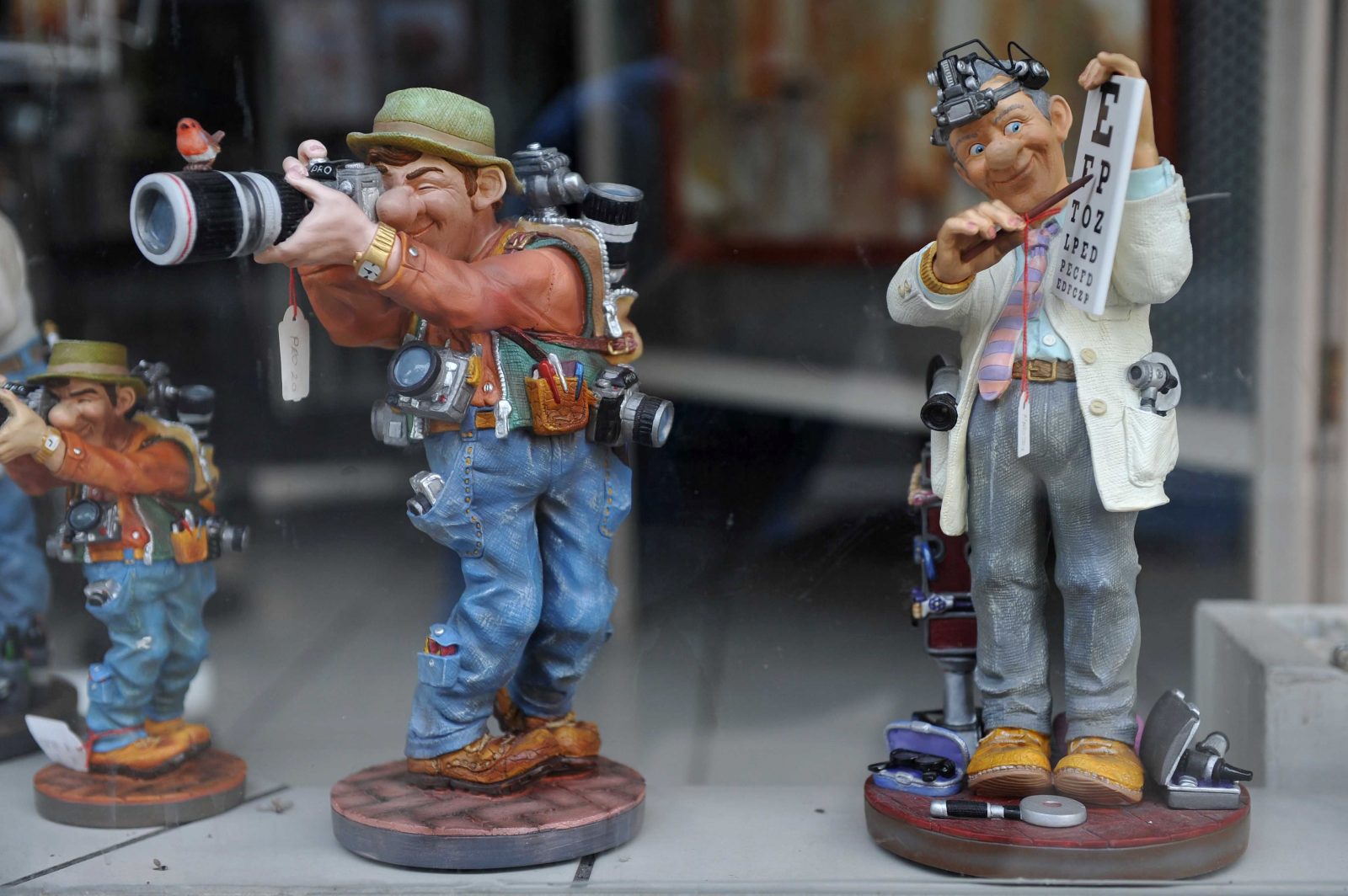 Two figurines stand in a shop window. One is an optomitrist, the other a caricature of a photographer. Photographed by Julian Stallabrass