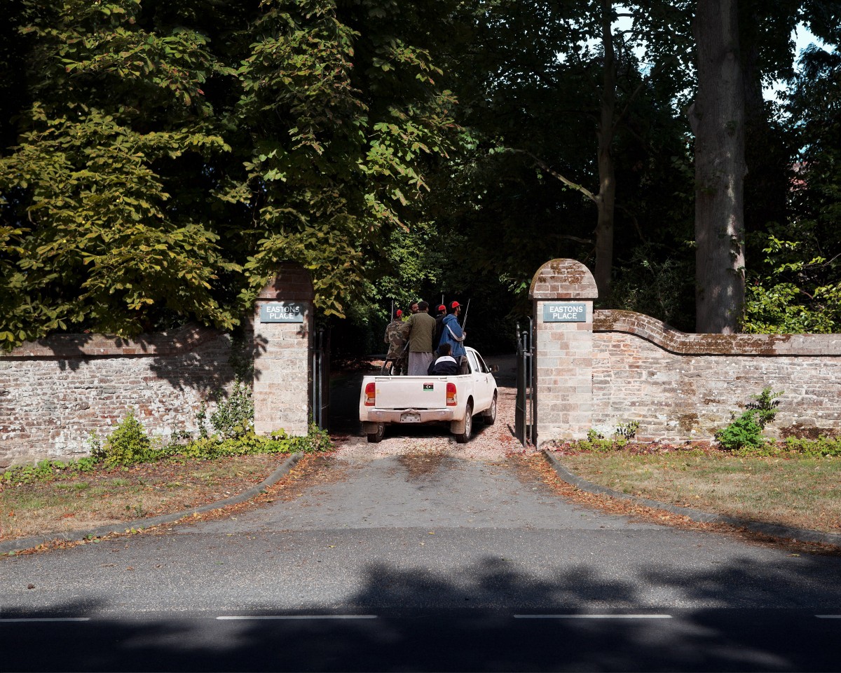 Young men in military dress with guns passing through gates of a rural English house