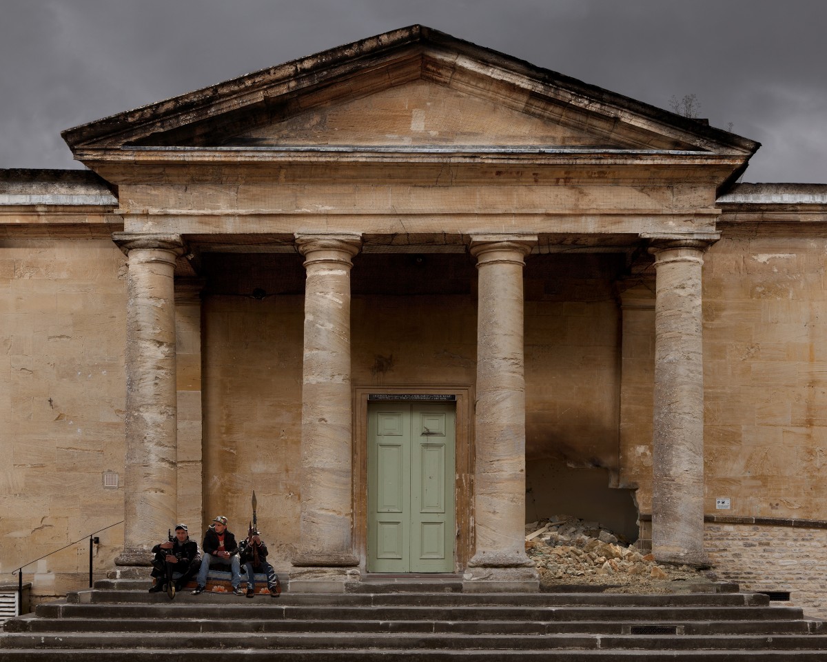 Young with men with guns sitting on steps of ruined building