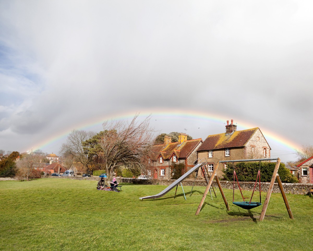 Rainbow, swing set and slides with men in headscarves sitting by tree